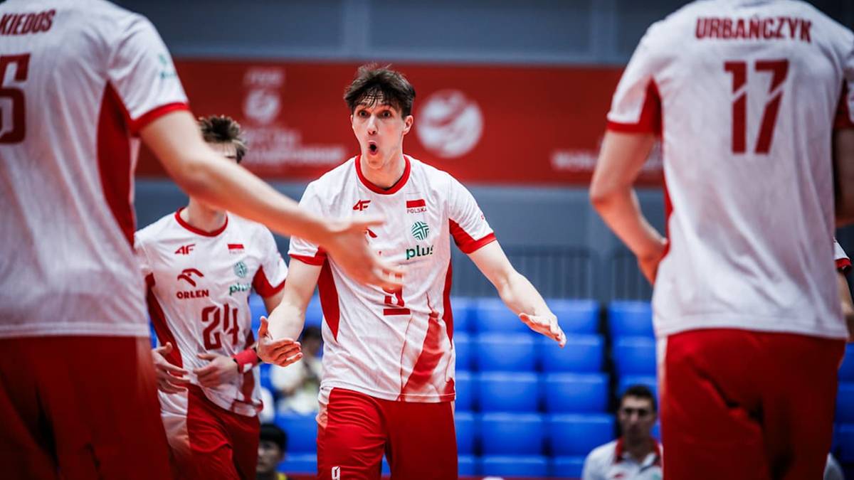 Siatkarz w białej koszulce z czerwonymi elementami, numerem 11 i nazwiskiem "Kaczmarek" na plecach, krzyczy podczas meczu, otoczony innymi zawodnikami.