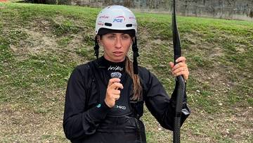 Klaudia Zwolińska w białym kasku i czarnym stroju sportowym, trzymająca mikrofon i wiosło.