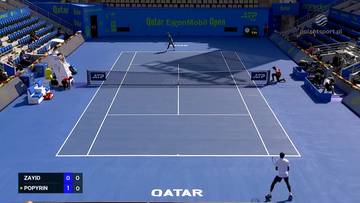 Kort tenisowy z niebieską nawierzchnią. Na boisku dwaj tenisiści w akcji. Na tablicy widnieje wynik meczu: Zayid 0, Popyrin 1.