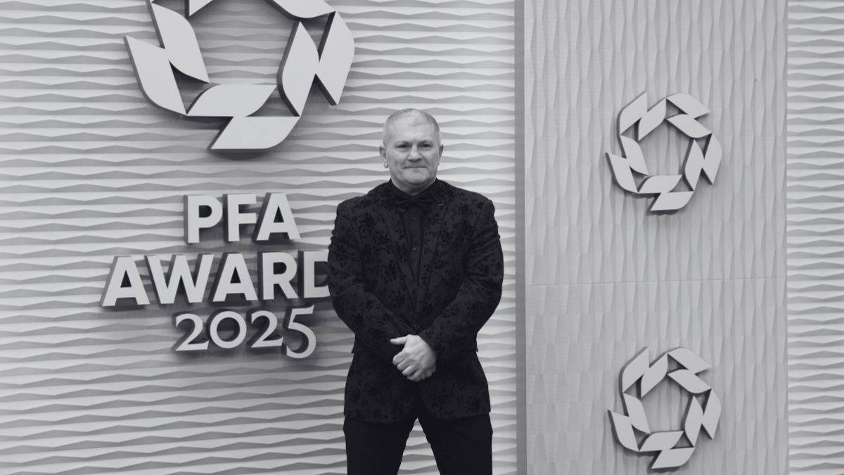 Mężczyzna w czarnym stroju stoi przed ścianą z napisem "PFA AWARD 2025" oraz dwoma stylizowanymi symbolami.