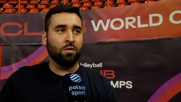 Portret Dominika Posmyka z brodą, ubranego w czarny t-shirt z logo Polsat Sport, podczas wywiadu.