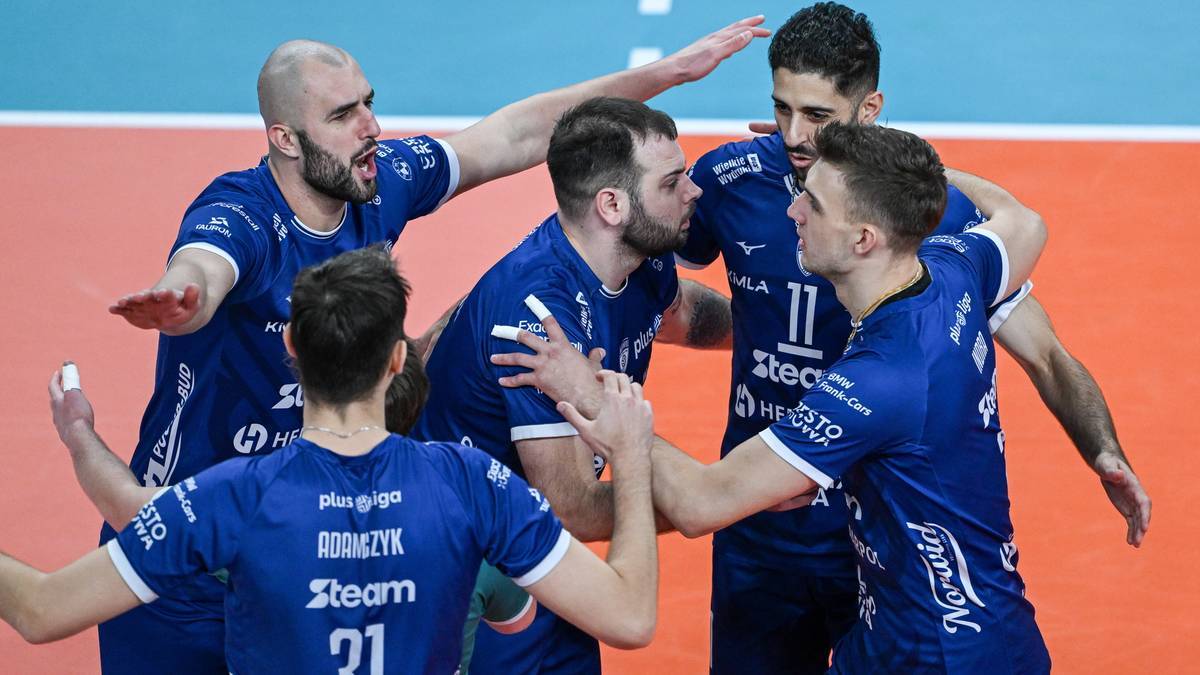Siatkarze w niebieskich strojach świętują razem na boisku siatkarskim.