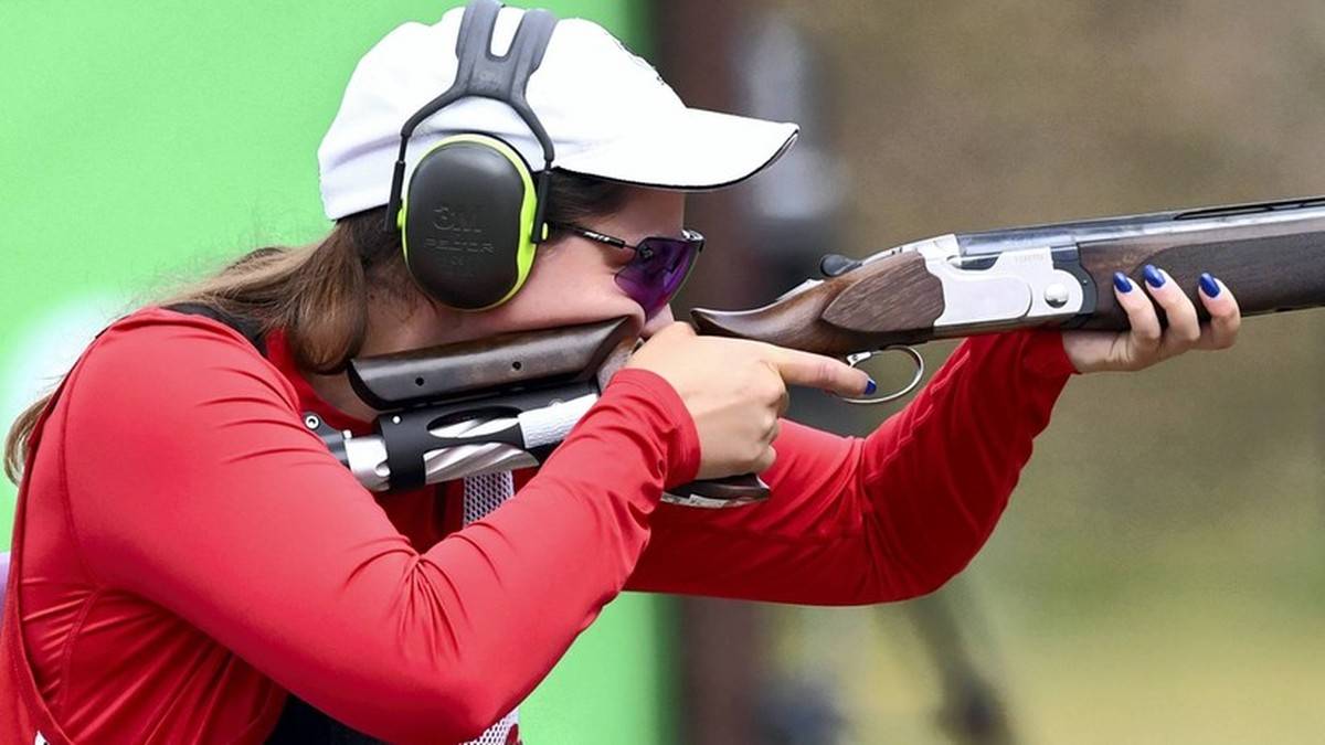 Kobieta w czapce i słuchawkach ochronnych celuje z broni palnej podczas zawodów strzeleckich.