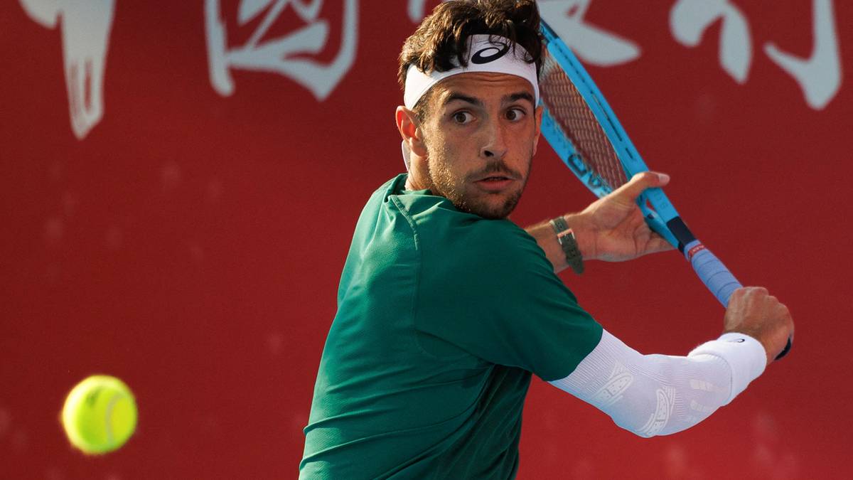 Tenisista w akcji podczas meczu z rakietą w ręku i piłką w locie.