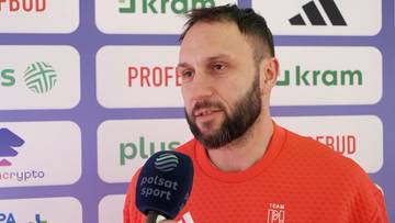 Portret Konrada Niedźwiedzkiego, mężczyzny z kr&oacute;tką brodą, w pomarańczowej koszulce, m&oacute;wiącego do mikrofonu.