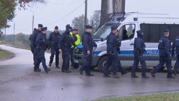 Grupa policjant&oacute;w w mundurach stojąca przy policyjnym busie zaparkowanym na poboczu drogi.