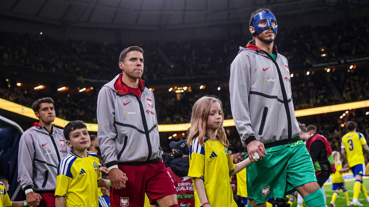 Piłkarze w szarych bluzach wychodzą na murawę stadionu, prowadząc dzieci.