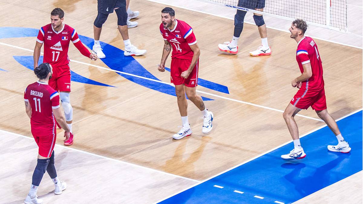 Grupa siatkarzy w czerwonych strojach rozgrywa mecz na drewnianym parkiecie kortu do siatkówki.