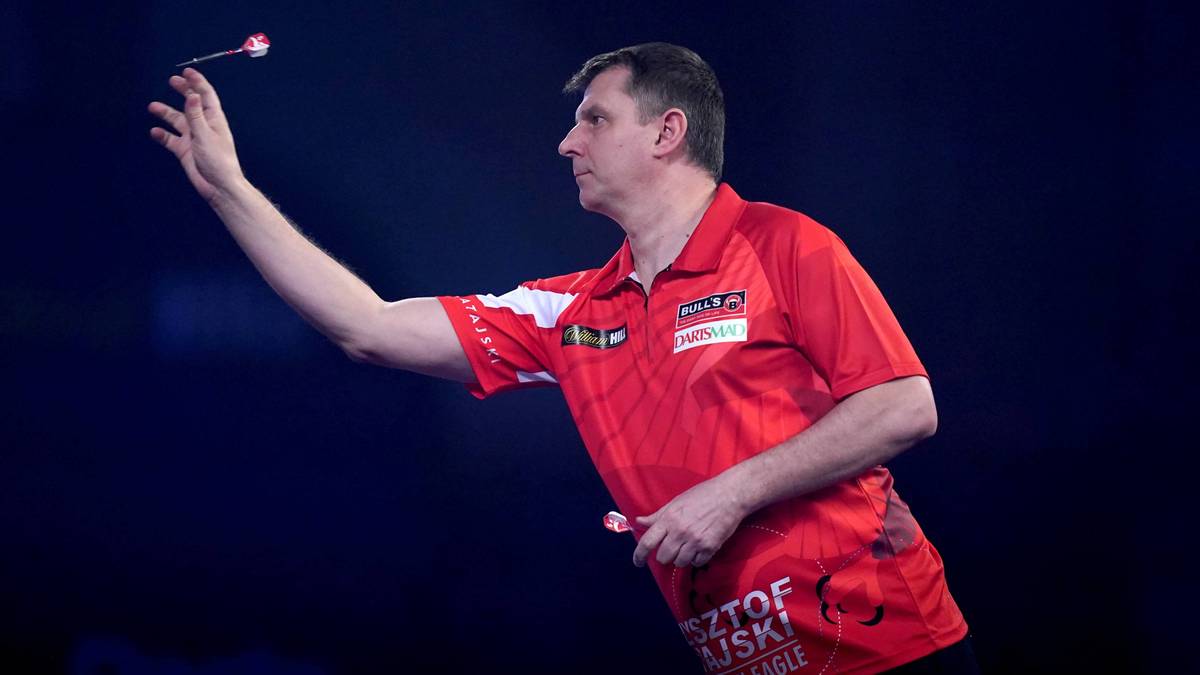 Mężczyzna w czerwonej koszulce sportowej wykonuje rzut rzutką.