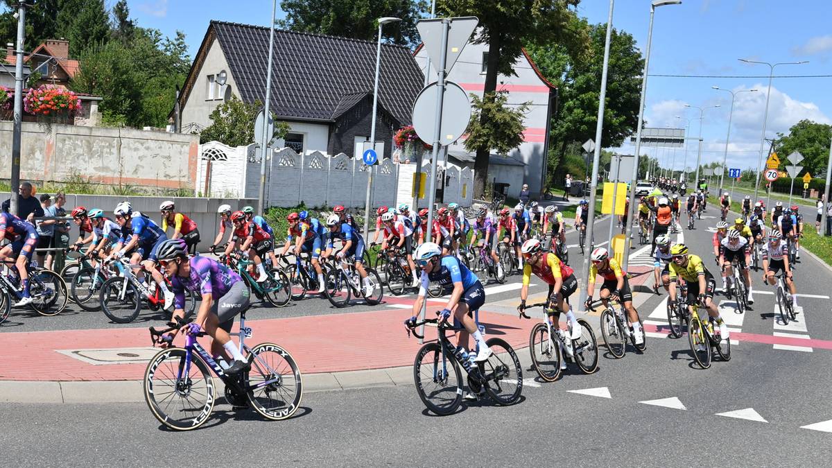 Grupa kolarzy na wąskiej drodze, jeden kolarz przewr&oacute;cony na asfalt.