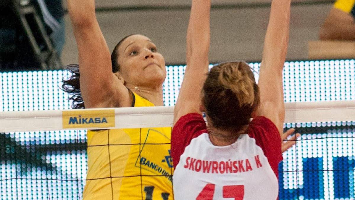 Dwie siatkarki rywalizujące o piłkę nad siatką, jedna w ż&oacute;łtej koszulce, druga w białej z czerwonymi elementami.