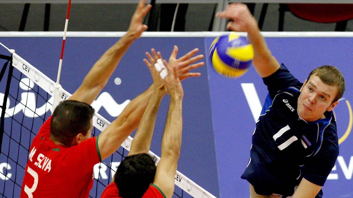 Siatkarz w niebieskiej koszulce wykonuje wysoki wyskok i uderza piłkę do siatk&oacute;wki w locie.