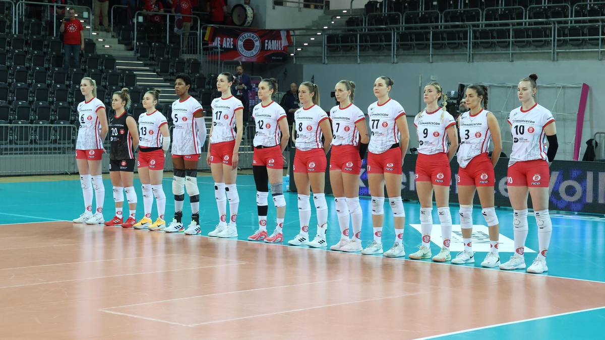 Drużyna siatkarek w strojach meczowych stoi w szeregu na boisku.