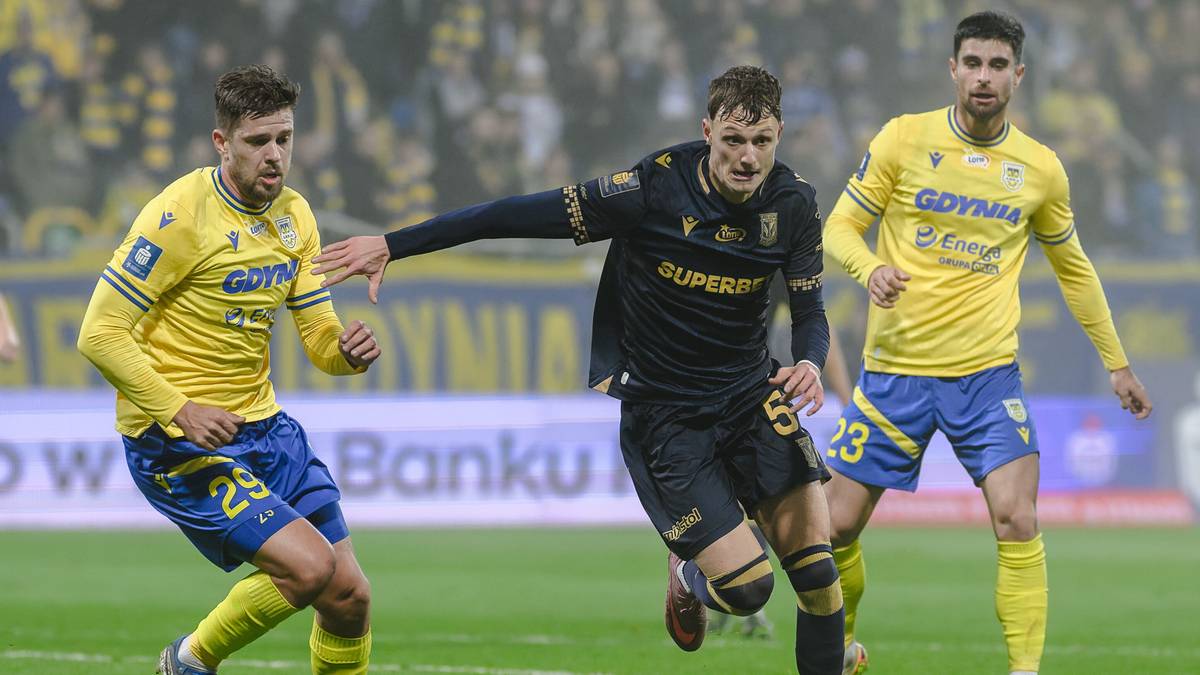 Trzech piłkarzy na boisku, dwóch w żółtych strojach, jeden w czarnym, podczas meczu piłkarskiego.