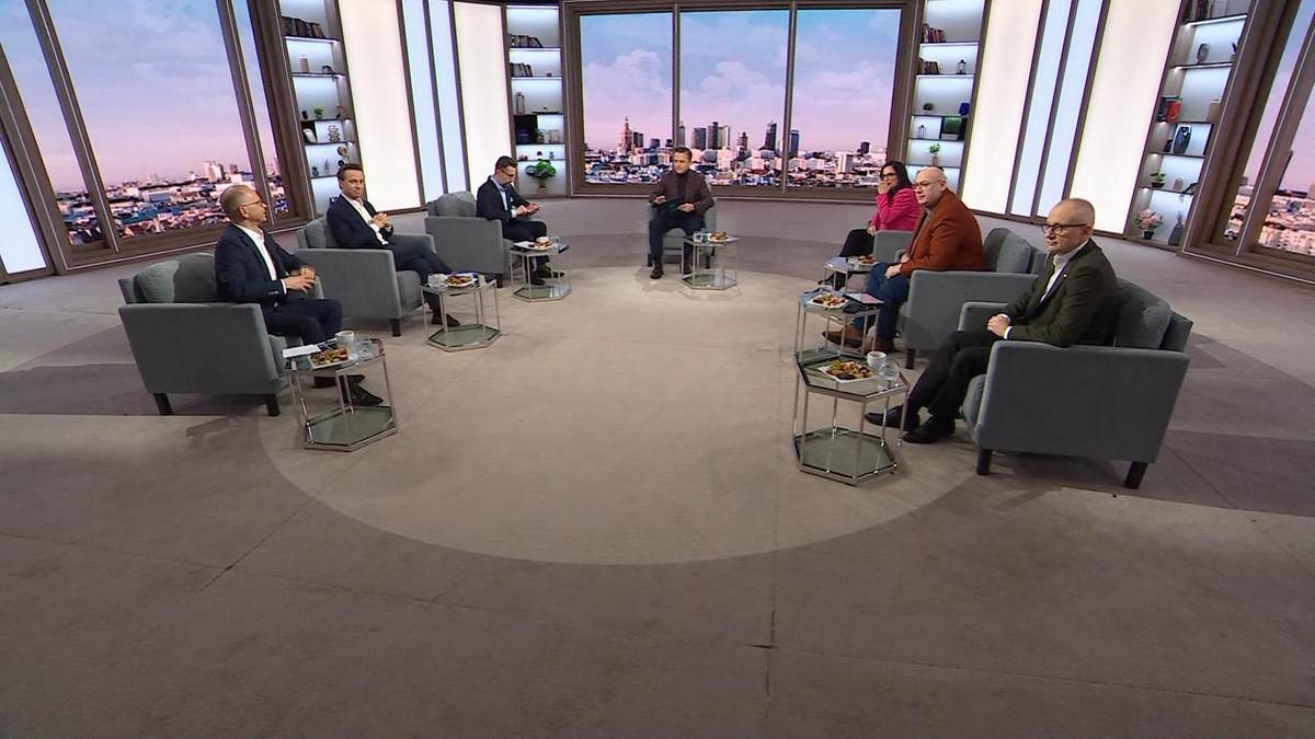 Siedem osób siedzi w okręgu na kanapach w studiu telewizyjnym, dyskutując.