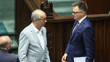 Dwóch polityków rozmawia w sali sejmowej, jeden w jasnej marynarce, drugi w granatowym garniturze.