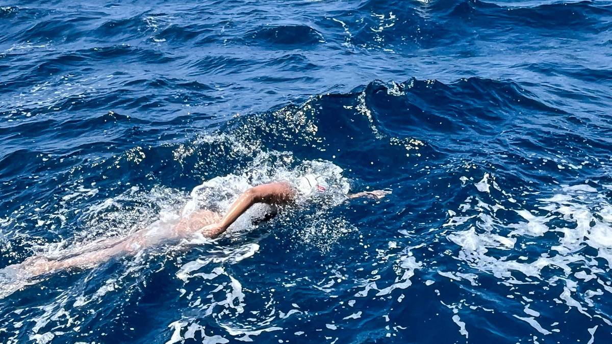 Kobieta płynąca w zimnej wodzie oceanu, z widocznym statkiem na horyzoncie.