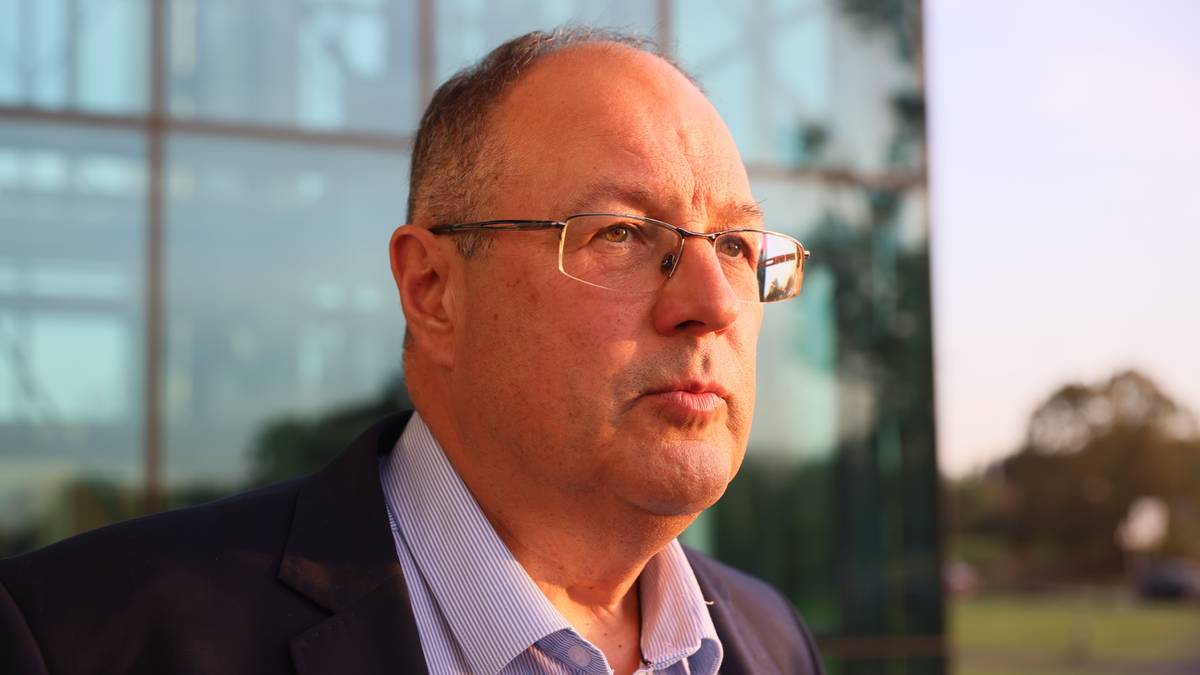 Portret mężczyzny w okularach, ubrany w ciemny garnitur i jasną koszulę. Mężczyzna ma kr&oacute;tkie, jasne włosy i spogląda w prawo.
