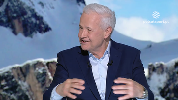 Apoloniusz Tajner w granatowym garniturze, uśmiechnięty, udziela wywiadu na tle górskiego krajobrazu.