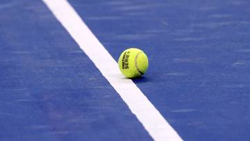 Piłka tenisowa leżąca na niebieskiej nawierzchni kortu obok białej linii.