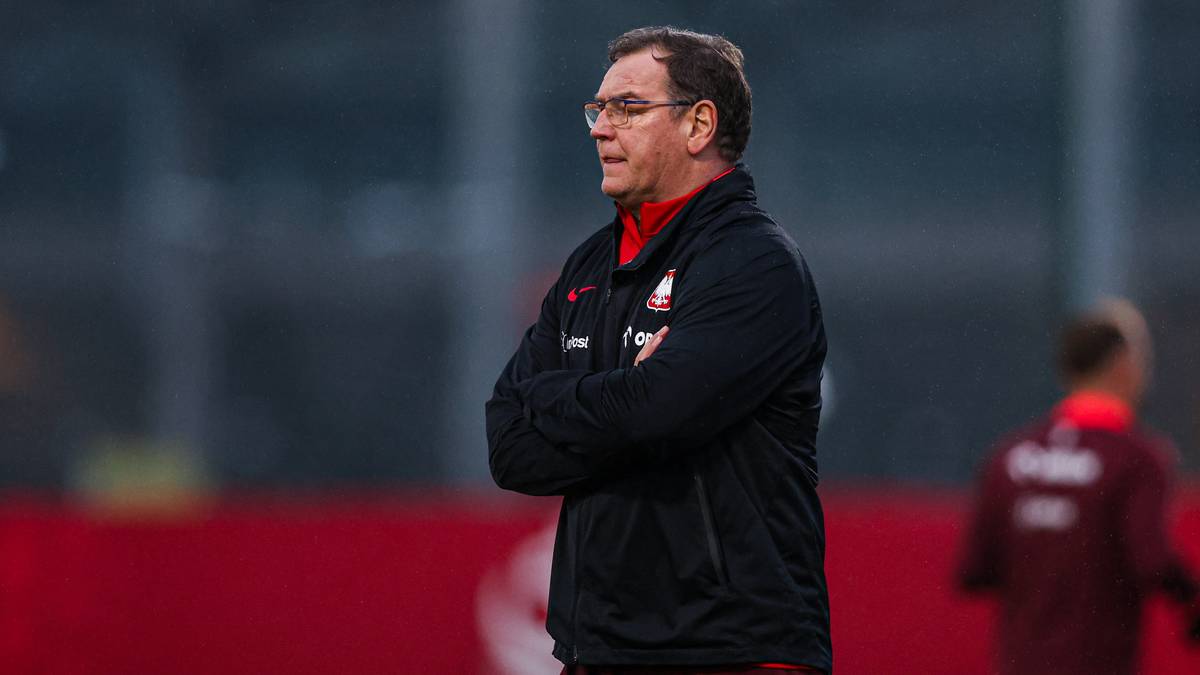 Portret mężczyzny w okularach, z rękami skrzyżowanymi na piersi, ubranego w czarną kurtkę z logo.