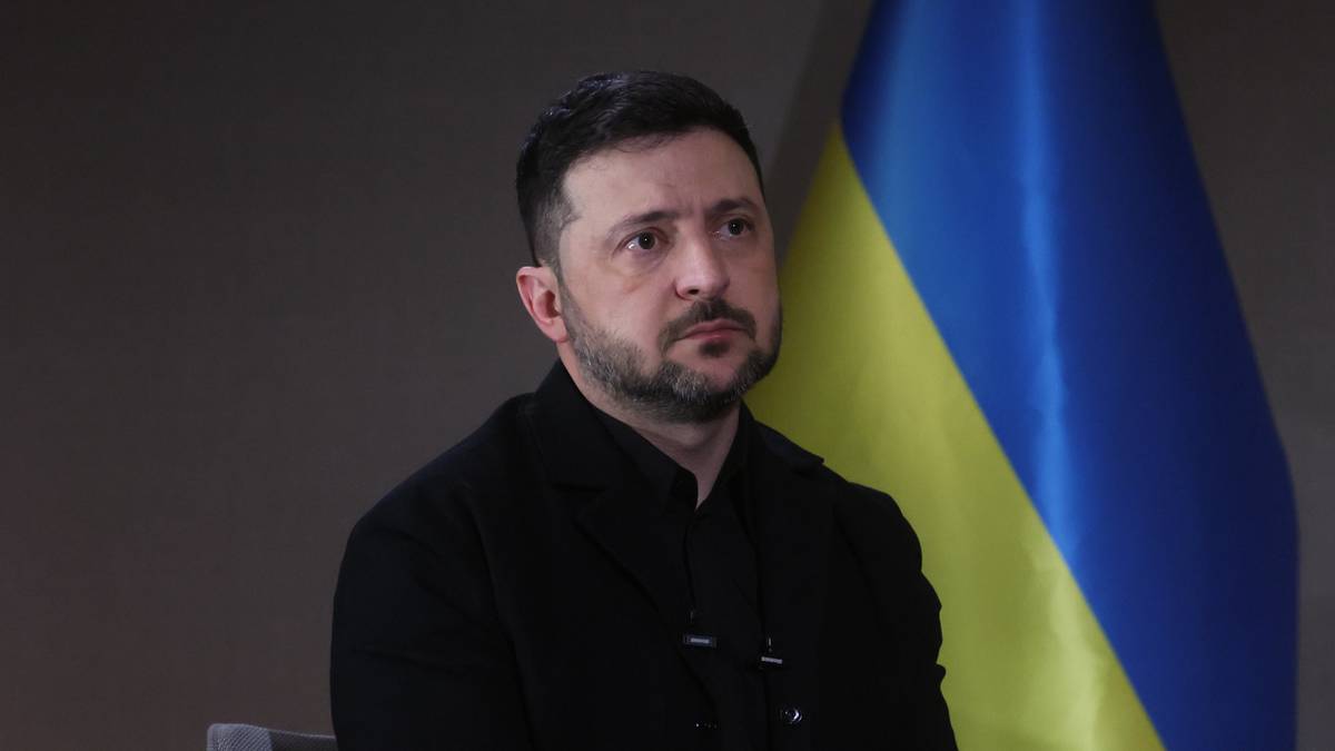 Wołodymyr Zełenski siedzi w fotelu przed flagą Ukrainy.