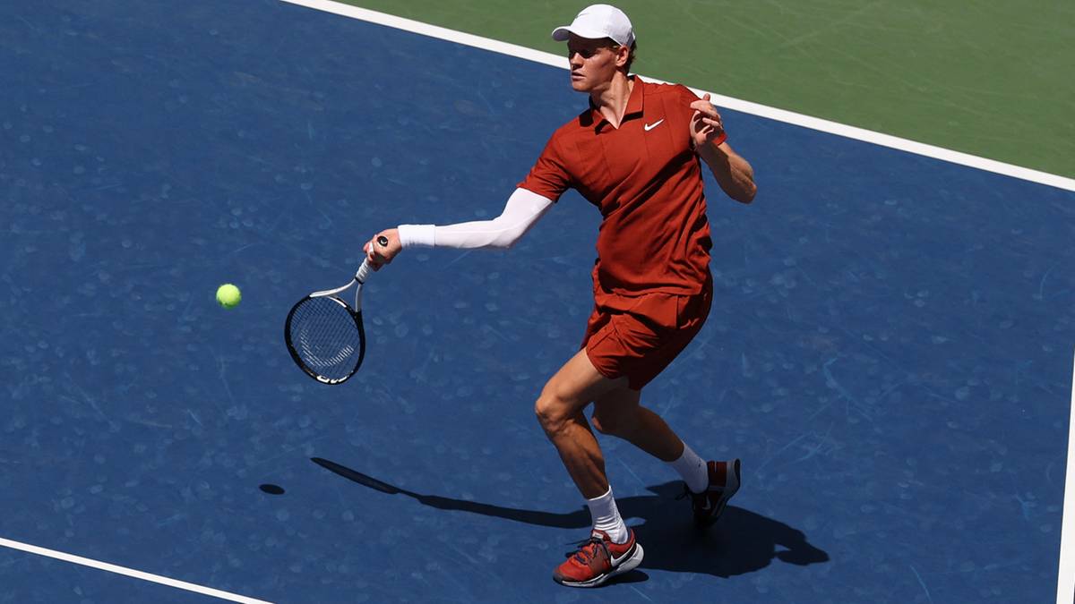 Mężczyzna w stroju tenisowym z rakietą uderza piłkę na korcie tenisowym.