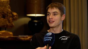 Młody mężczyzna z kr&oacute;tkimi jasnymi włosami, udzielający wywiadu z mikrofonem Polsat Sport, ubrany w czarną koszulkę.