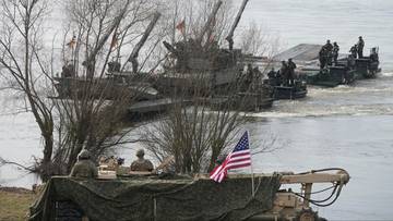 Żołnierze amerykańscy budują most pontonowy na rzece z użyciem ciężkiego sprzętu wojskowego.