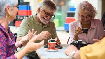 Grupa starszych os&oacute;b przy stoliku z kawą i aparatem