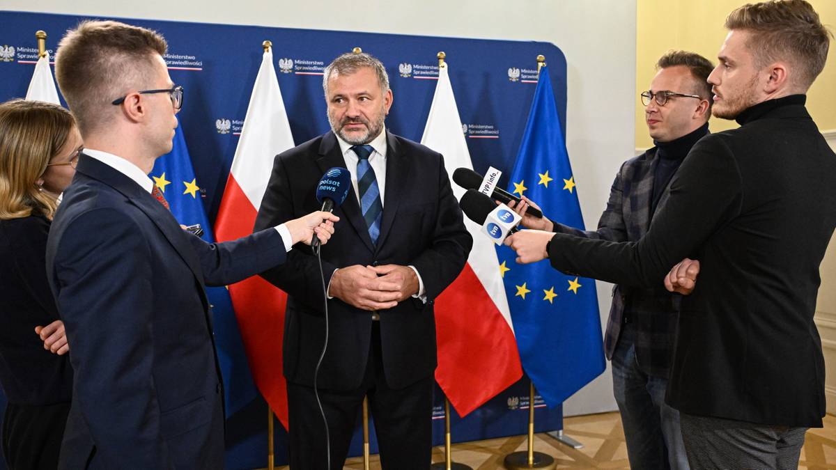 Minister sprawiedliwości Waldemar Żurek podczas konferencji prasowej w otoczeniu dziennikarzy z mikrofonami.