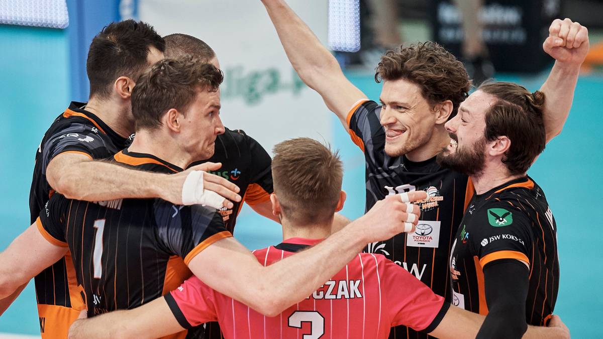 Grupa siatkarzy w strojach sportowych ściska się i cieszy po zwycięstwie lub udanej akcji. Ich twarze wyrażają radość i entuzjazm.