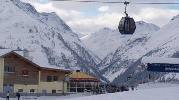 Ośnieżone g&oacute;ry z kolejką gondolową i budynkami przy trasie narciarskiej.