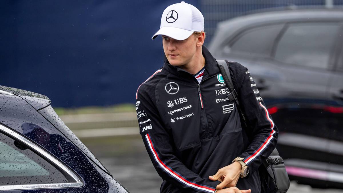 Młody kierowca w czapce z daszkiem i kurtce zespołu Mercedes patrzy w dół.