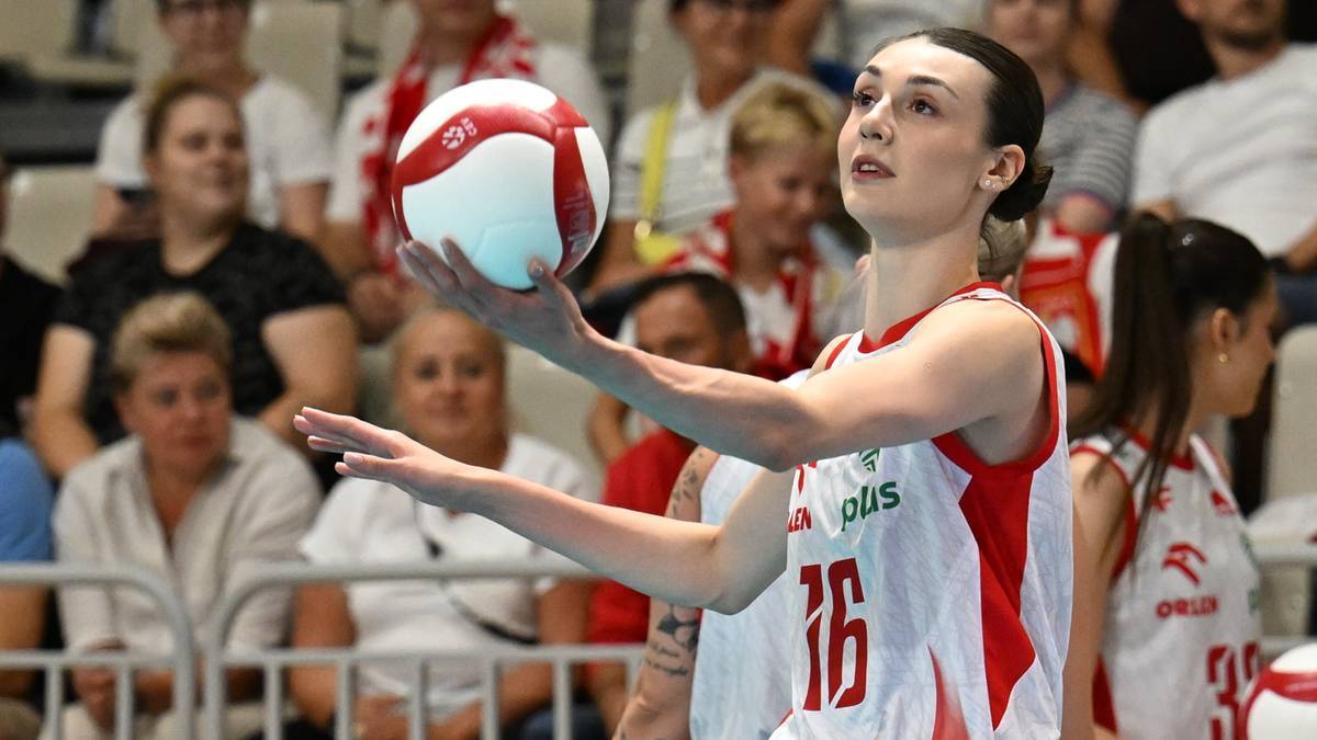 Zawodniczka siatkówki w czerwono-białej koszulce z numerem 16 przygotowuje się do zagrywki, trzymając piłkę w prawej dłoni.