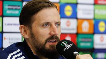 Trener Marek Pachniak podczas konferencji prasowej m&oacute;wi do mikrofonu.
