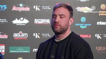 Portret mężczyzny z zamkniętymi oczami i zarostem, na tle ściany z logotypami.