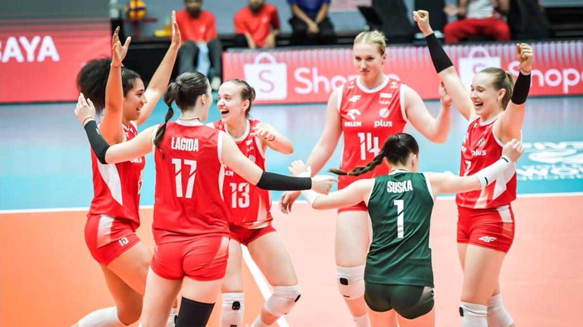 Grupa siatkarek w czerwonych strojach świętuje zwycięstwo, przytulając się i podnosząc ręce w geście radości.