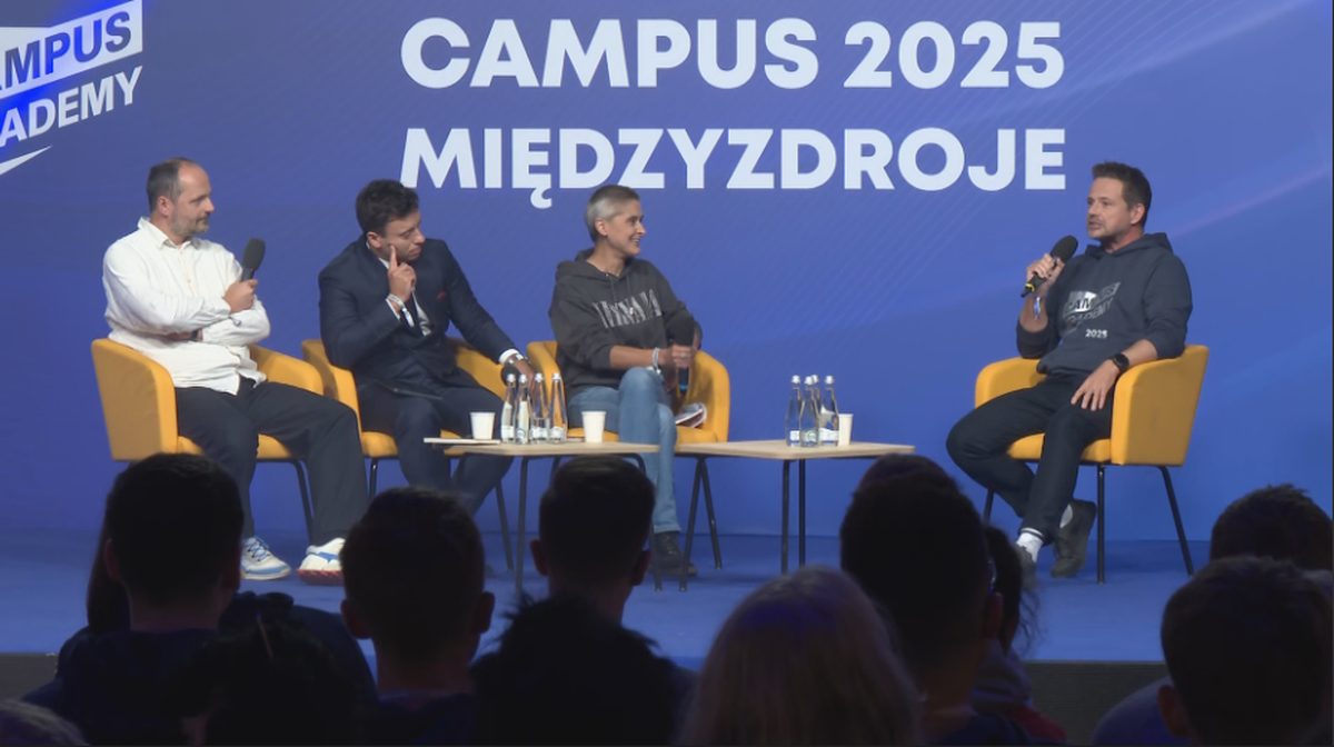 Czterech mężczyzn i jedna kobieta siedzą na żółtych krzesłach przed stolikiem z wodą. Na ekranie w tle widnieje napis "CAMPUS 2025 MIĘDZYDROJE". Jeden z mężczyzn trzyma mikrofon i mówi, prawdopodobnie udzielając wywiadu.
