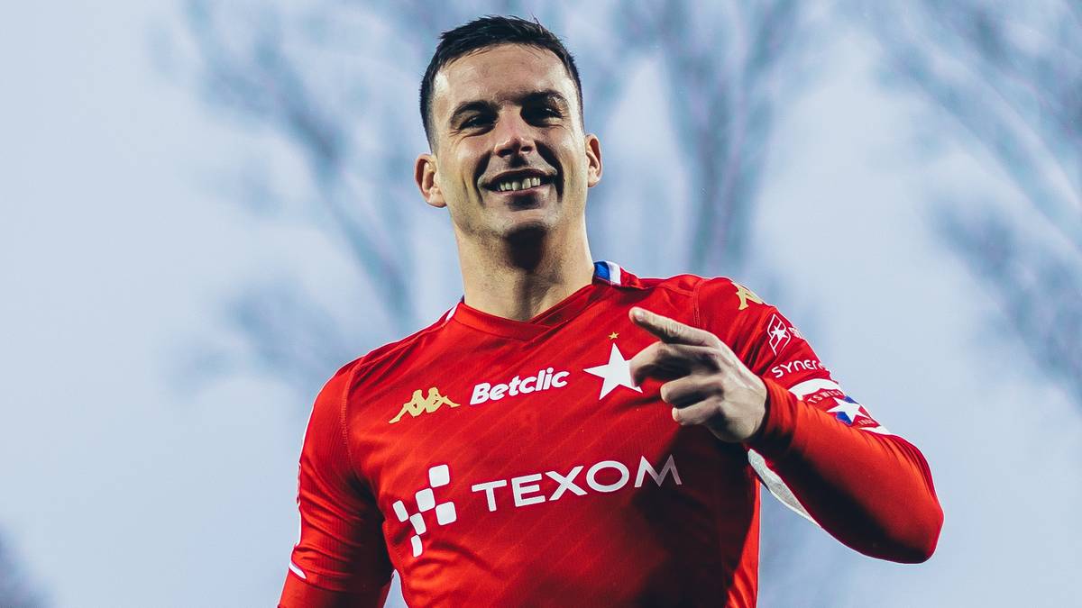 Piłkarz w czerwonej koszulce z numerem 9 i logo Texom biegnie po boisku stadionu.