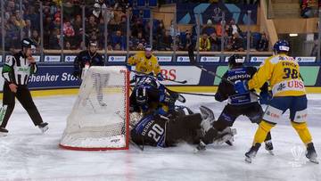 Sędzia i zawodnicy hokejowi w akcji pod bramką podczas meczu.