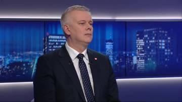 Mężczyzna w garniturze i krawacie siedzi w studiu telewizyjnym, patrząc w bok.