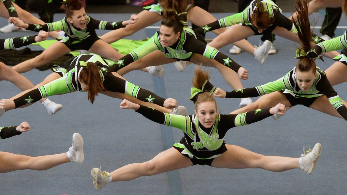 Grupa cheerleaderek w strojach sportowych wykonuje akrobatyczne figury podczas występu.
