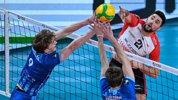 Trzech siatkarzy walczy o piłkę pod siatką podczas meczu siatk&oacute;wki.