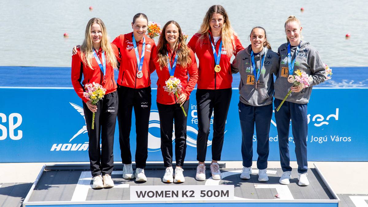 Pięć kobiet w strojach sportowych stoi na podium, trzymając medale. Dwie z nich mają na szyjach medale, a pozostałe trzy trzymają kwiaty.