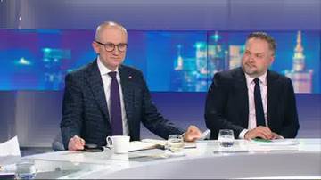 Dw&oacute;ch mężczyzn w garniturach siedzi przy stole w studiu telewizyjnym.