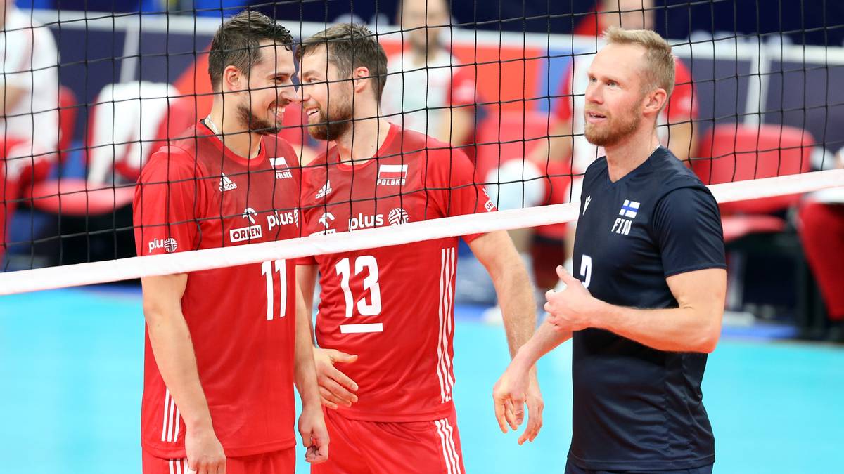 Trzech siatkarzy przy siatce, dw&oacute;ch w czerwonych strojach, jeden w granatowej koszulce z napisem FIN
