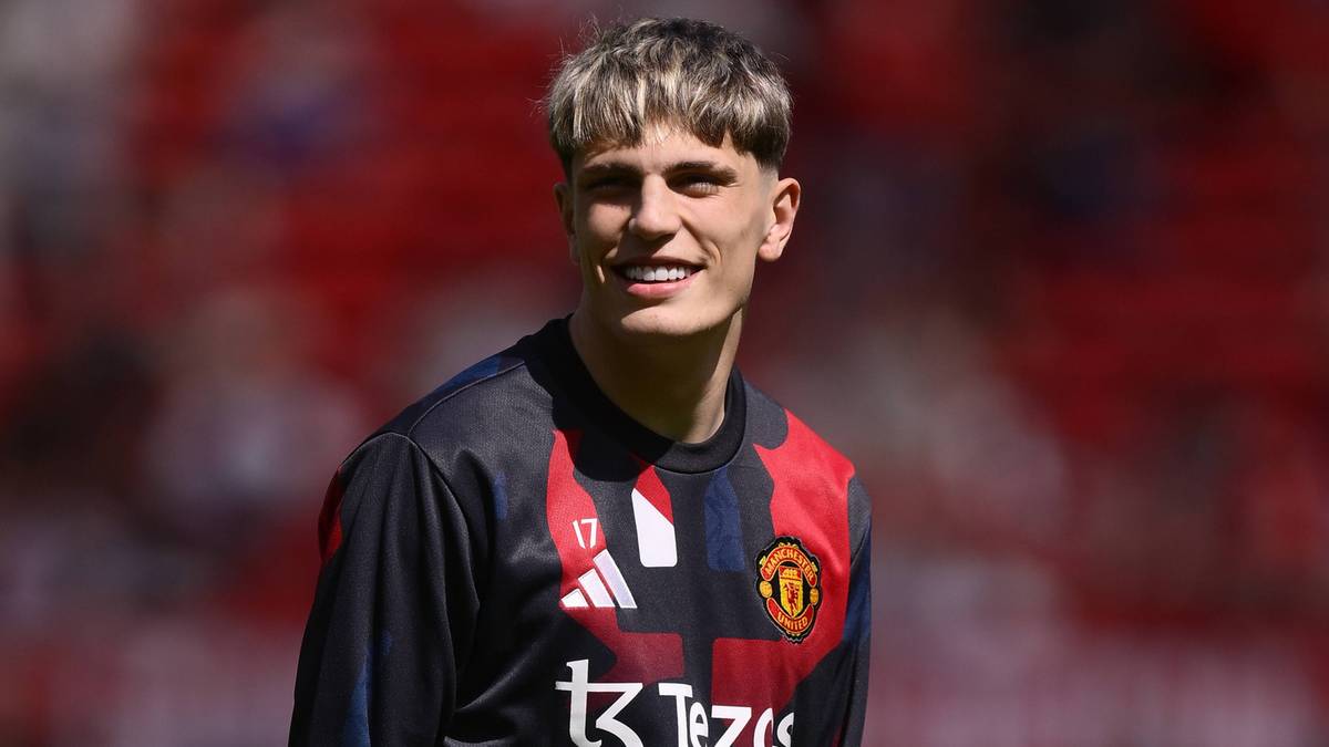 Młody mężczyzna w stroju piłkarskim z herbem Manchesteru United, lekko się uśmiecha.