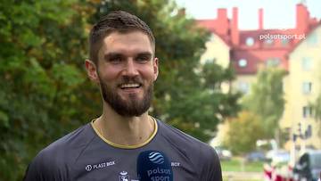Karol Kłos uśmiecha się podczas udzielania wywiadu w sportowej koszulce.