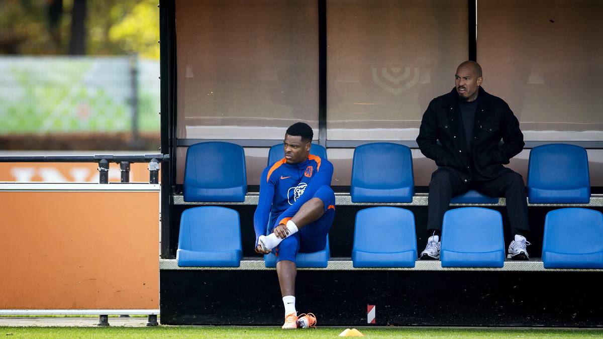 Dwóch piłkarzy siedzi na ławce rezerwowych na boisku piłkarskim.